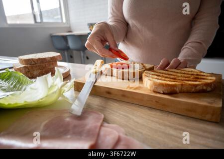 Preparazione di un panino con prosciutto e formaggio grigliato con ingredienti freschi a casa Foto Stock