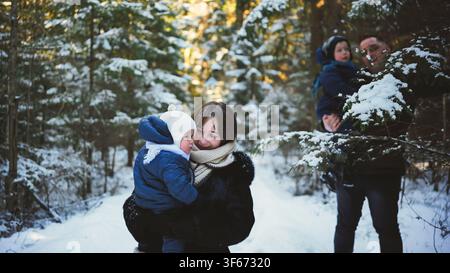 Famiglia felice che cammina in una bellissima foresta invernale, godendosi la natura innevata e divertendosi in una giornata invernale soleggiata Foto Stock