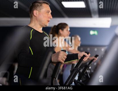 Uomo sportivo e forte che utilizza una macchina ellittica in palestra Foto Stock