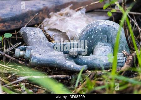 Primo piano di una pistola a spruzzo per vernici abbandonata a terra con gocce di vernice sparse ovunque e uno sfondo verde morbido Foto Stock