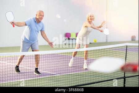 Coppia di donne anziane e uomini che giocano a doppio pickleball al coperto Foto Stock