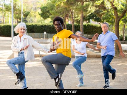 Gli anziani felici e le persone di mezza età che si allenano insieme ballano in un parco soleggiato Foto Stock