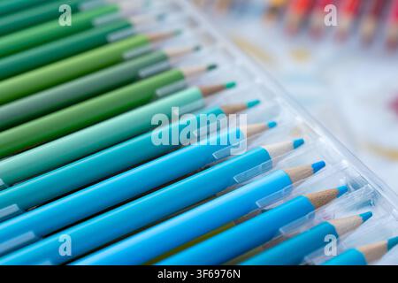 Un primo piano macro dettagliato che si concentra su una selezione di matite colorate blu, turchesi e verdi disposte ordinatamente all'interno di un vassoio di plastica trasparente Foto Stock