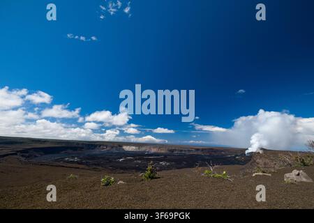 Scattata dall'Uekahuna Overlook all'interno del Parco Nazionale dei Vulcani delle Hawaii, questa veduta mostra la vasta caldera di Kīlauea sotto un cielo hawaiano luminoso. Foto Stock