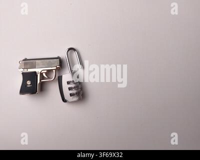 Un modello in miniatura di pistola posizionato accanto a un lucchetto a combinazione aperto su una superficie beige. Foto Stock