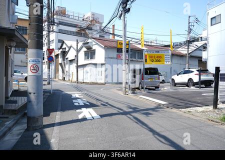 Un incrocio stradale accanto a un parcheggio di monete senza contanti con cartelli dei prezzi e auto parcheggiate in una giornata soleggiata a Tokyo, Giappone. Foto Stock