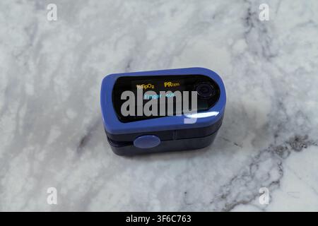 Un oximetro di impulsi blu che mostra Dito fuori su una superficie di piano di marmo Foto Stock