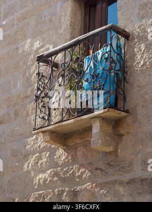 Balcone in ferro battuto ornato con biancheria e pianta sulla facciata in pietra di granito antica di un edificio, Olbia, Sardegna Foto Stock