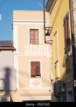 Facciate di edifici intonacati di pesca e giallo con finestre a persiane di legno, lampione e pannello solare, Olbia, Sardegna, Italia Foto Stock
