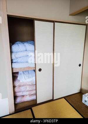 Tottori, Giappone – 18 giugno 2026: Biancheria da letto tradizionale giapponese (futon) accuratamente piegata e riposta in un armadio scorrevole in una camera degli ospiti di un ryokan a Hawai On Foto Stock
