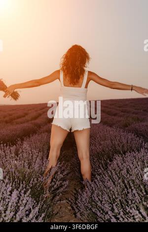 Donna nel campo di lavanda libertà in piedi con le braccia aperte in un paesaggio viola in fiore durante il tramonto con una luce calda e soffusa Foto Stock
