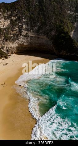 Vista aerea di Kelingking Beach con onde turchesi che si infrangono sulla riva sabbiosa, incorniciata da ripide scogliere di calcare a Nusa Penida, Bali, Indonesia. Foto Stock