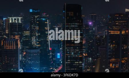 Vista aerea dei grattacieli illuminati nella fitta skyline urbana di notte a Jakarta, Indonesia. Foto Stock