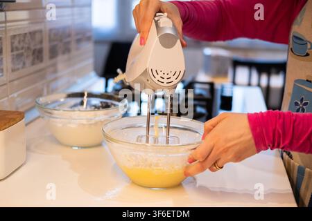 Persona che prepara cibo, utilizza un mixer elettrico a mano per mescolare l'impasto in una ciotola Foto Stock