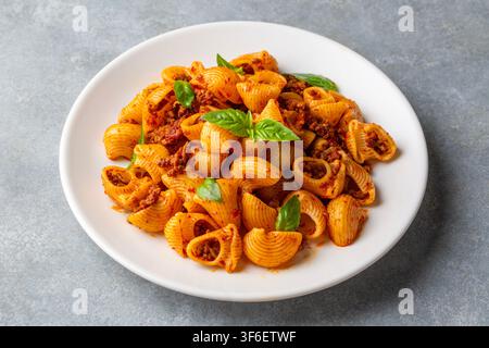 Deliziosa pasta Pipe Rigate con salsa bolognese di carne e foglie di basilico fresco Foto Stock
