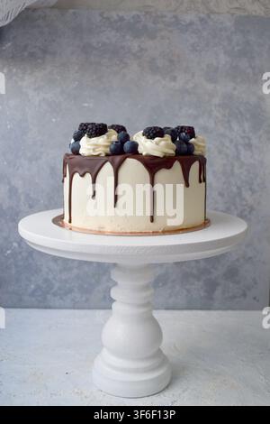Torta a gocce bianca con ganache al cioccolato, spirali di panna montata, mirtilli e more su supporto Foto Stock