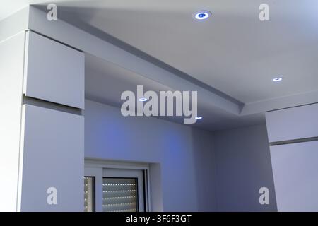 Una stanza contemporanea presenta eleganti armadi bianchi e un soffitto a gradini con una sottile illuminazione a LED blu come accento Foto Stock