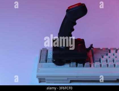 Joystick retrò su vecchia tastiera PC. Luce neon sfumata rosso-blu. Attributi degli anni '80, gaming. Onde retrò Foto Stock