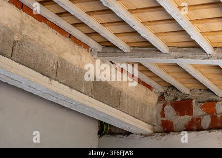 Vista ravvicinata di un edificio in costruzione, che mette in evidenza travi in cemento, muri di mattoni a vista e travi del soffitto in legno Foto Stock