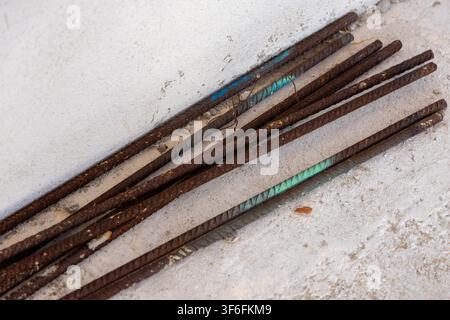 Vista ravvicinata di barre di acciaio arrugginite con ruggine visibile e alcuni segni colorati, appoggiate su cemento ruvido Foto Stock