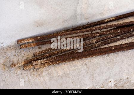 Prima vista di barre d'acciaio consumate con una texture di ruggine prominente appoggiate su uno sfondo di cemento ruvido, che suggerisce degrado o materiali da costruzione Foto Stock