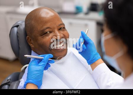 Ritratto ravvicinato di un paziente anziano nero sorridente che tiene uno strumento specchio dentale Foto Stock