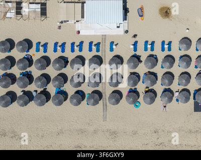 Vista aerea di Kriaritsi Beach con file di ombrelloni di paglia e lettini blu sulla riva sabbiosa, dove le persone si rilassano in Grecia. Foto Stock