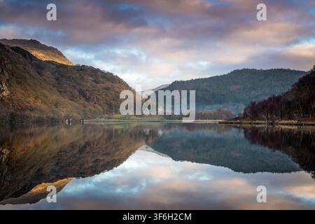 Riflessi mattutini mozzafiato di montagne e un cielo drammatico sulla superficie calma del lago Llyn Dinas nel Parco Nazionale di Eryri, Galles del Nord. Spazio di copia Foto Stock