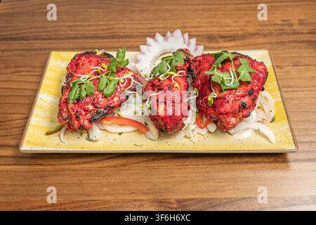 Pezzi di pollo tandoori arrostiti guarniti con coriandolo e germogli su un letto di cipolle Foto Stock