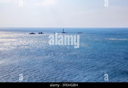 Una vista da Land’s End, Cornovaglia, che guarda verso il faro di Longships in posizione maestosa su affioramenti rocciosi nell’Oceano Atlantico Foto Stock