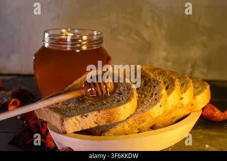 Miele dorato gocciola su una fetta di pane fresco. Pasto della colazione mattutina con sciroppo dolce, crema spalmabile cremosa. Quadrato di toast croccante si trova sul tavolo della cucina accanto a g Foto Stock