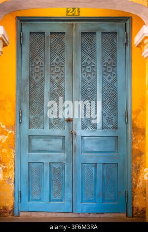 Ingresso vintage ad un edificio con vecchia porta doppia in legno chiusa dipinta di blu su muro giallo Foto Stock