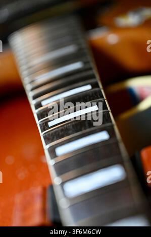Fotografia verticale in primo piano di una tastiera di chitarra con enfasi sulle corde metalliche e sulle intarsi bianchi rettangolari di posizionamento, su un corpo di strumento in legno sfocato, che mette in risalto i dettagli e la texture Foto Stock