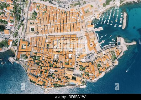 Fotografia aerea della Città Vecchia di Dubrovnik in Croazia che mostra le mura storiche della città, i tetti coperti di tegole arancioni, le strade strette e il porto adiacente con numerose barche ormeggiate nel mare Adriatico turchese. Foto Stock