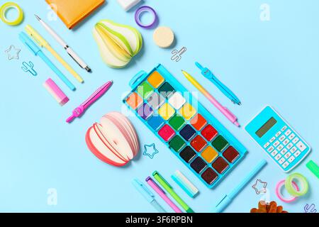 Materiali scolastici e per ufficio colorati con set di pittura ad acquerello e calcolatrice su uno sfondo blu chiaro Foto Stock