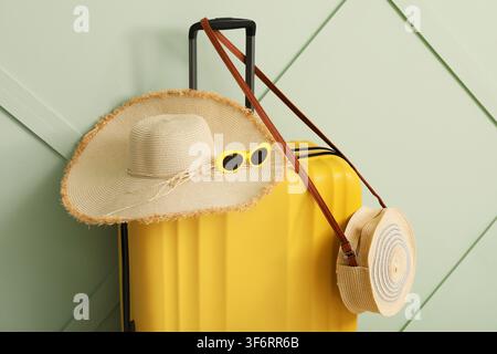 Valigia gialla con un cappello di paglia a tesa larga, occhiali da sole e una piccola borsa di paglia, pronta per i viaggi estivi Foto Stock