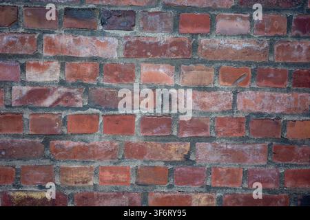 La scena mostra un muro di mattoni composto da mattoni rossi e marroni. I mattoni sono disposti secondo uno schema regolare. Questo tipo di muro è comune negli ambienti urbani Foto Stock