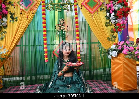 Giovane donna indiana in lehenga tradizionale verde seduta durante la cerimonia del mehndi con piatto di henné, decorata con drappi gialli e verdi e motivi floreali indiani Foto Stock