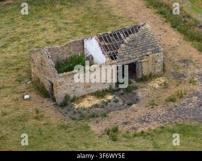 Vista aerea di un edificio rurale in pietra abbandonato con un tetto parzialmente crollato, situato nella campagna aperta vicino a Birkenshaw Bradford, circondato da secco Foto Stock