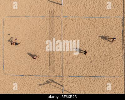 Vista aerea dall'alto di giocatori in competizione in una partita di beach volley su un campo di sabbia con ombre drammatiche, concetto di sport estivo all'aperto. Foto Stock