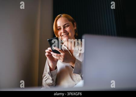 Giovane donna felice che sorride al suo smartphone Foto Stock