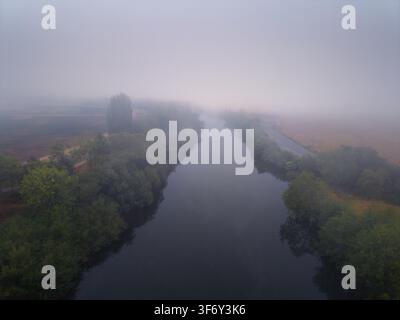 Vista aerea del fiume Coquille che scorre attraverso un paesaggio avvolto da una fitta nebbia mattutina, con alberi rigogliosi e campi lungo le rive a Coquille, Or Foto Stock