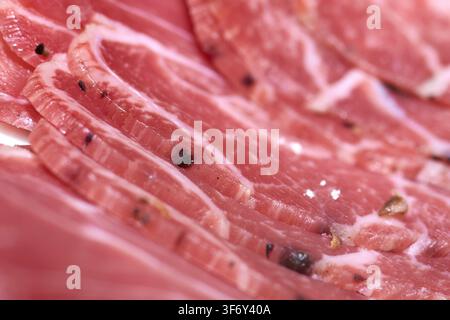 Macro primo piano di prosciutto affumicato e salame affettati sottilmente disposti su un piatto, conditi con grani di pepe nero interi e fiocchi di sale marino per un appeti Foto Stock
