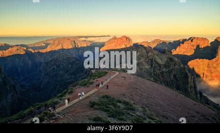 Juncal, Portogallo - 05.12.2025: Vista panoramica di escursionisti che attraversano una cresta montuosa rocciosa durante il tramonto con ombre drammatiche e nuvole basse Foto Stock