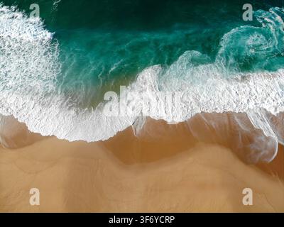 Una fotografia aerea dall'alto cattura una bellissima spiaggia di sabbia deserta che incontra chiare onde turchesi dell'oceano con schiuma bianca. Foto Stock