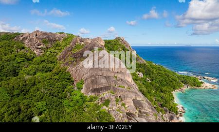 Picchi di granito che si innalzano sopra una fitta vegetazione verde con un cielo sereno sullo sfondo. Seychelles, La Digue. Foto Stock