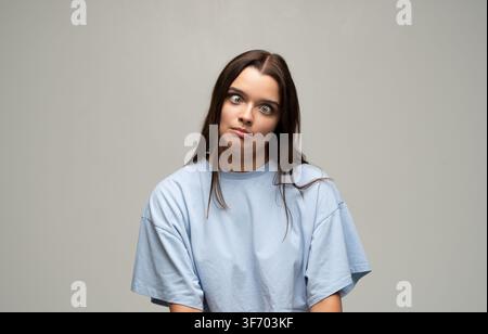 Giovane donna che fa una faccia buffa, confusa e strabica, esprimendo sciocchezza, umorismo e sorpresa in uno studio Foto Stock