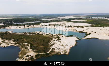 Paesaggio industriale di cava artificiale con colline sabbiose e laghi di acqua turchese visti dall'alto Foto Stock