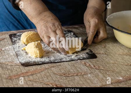 Una vista ravvicinata di mani consumate che tagliano l'impasto di formaggio fresco per syrniki, illustrando il processo autentico di preparazione dei tradizionali fo dell'Europa orientale Foto Stock