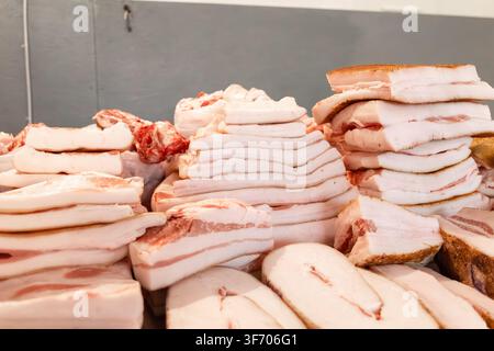 File di lardo di maiale crudo a fette e pancetta salata sono impilate su un tavolo in una macelleria, mostrando ingredienti artigianali di alta qualità essenziali per la tradizione Foto Stock